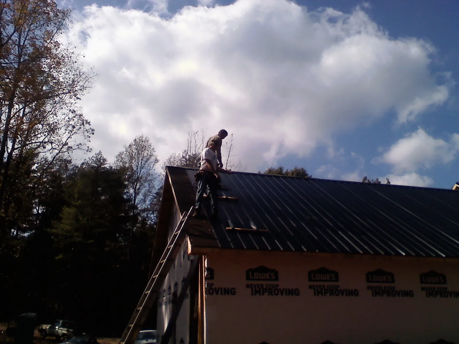 Roofer fastening dark metal panels high against a cloudy sky, from a Roof Inspection job in Lee